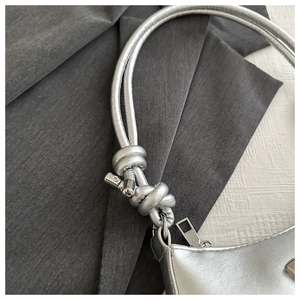 Close-up of silver handbag shoulder strap featuring double-cord knot and metal hardware