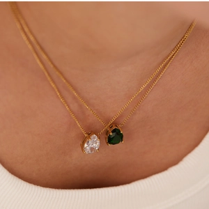 Close-up of teardrop emerald and white zircon pendant necklace on woman's collarbone