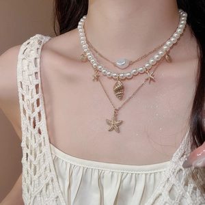 Macro shot of gold starfish and conch pendants on layered pearl necklace set