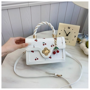 Detail of white cherry print handbag featuring floral gold lock and twisted top handle