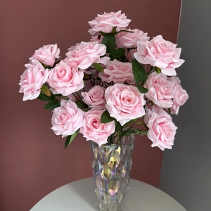 Close-up of pink artificial roses in a shimmering glass vase on a white round table