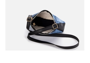 Close-up of blue denim underarm bag with black leather trim and golden metal hardware