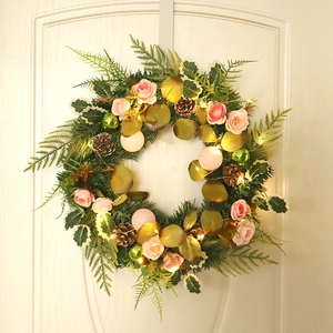 Pink rose Christmas wreath with LED lights and pine cones hanging on a beige front door