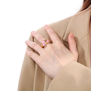 Detailed shot of golden enamel ring with pink polka dots worn on a khaki blazer