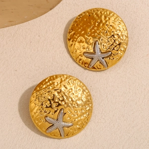 Detail of round hammered gold stud earrings featuring a silver starfish center piece