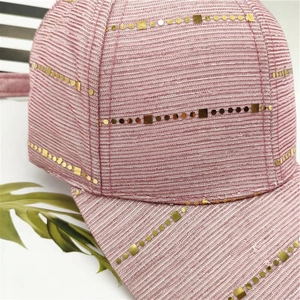 Close-up of pink textured fabric baseball cap with golden sequins and metal studs