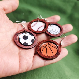 Hand hält runde Sportohrringe aus Holz mit Fußball- Baseball- Volleyball- und Basketballmotiv