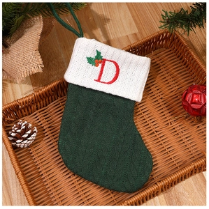 Green knitted Christmas stocking with white cuff and red letter D in a cozy gift basket