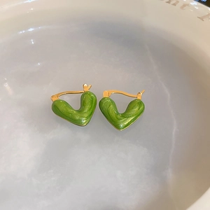 Detail view of green enamel heart earrings with gold trim in a water reflection setting