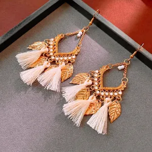 Bohemian leaf earrings with gold finish and cream tassels displayed on a grey tray