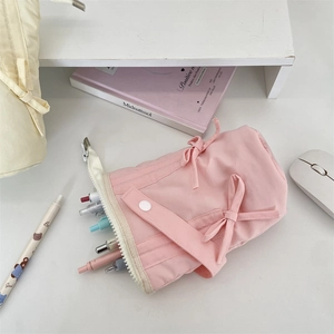 Pink fabric pencil case with decorative bows and colorful pens inside on a white desk