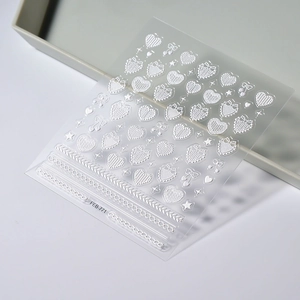 Macro detail of white 3D embossed nail stickers with bows hearts and lace patterns