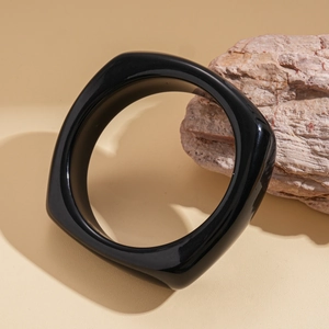 Macro shot of polished black square acrylic bangle on a natural stone textured background