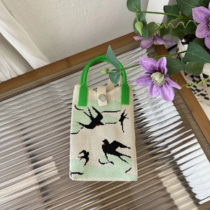 Detail of knitted bird pattern handbag with green handle and secure metal snap closure