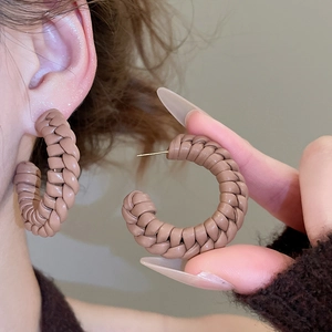 Detail of coffee brown hand-woven leather C-shaped hoop earrings with gold pins