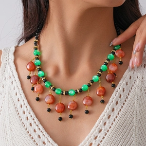 Close-up of bohemian beaded necklace with green and red resin beads on gold chain