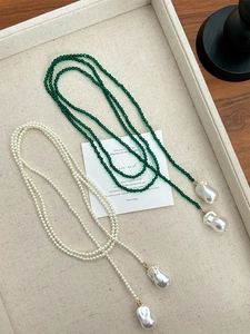 Detail of long layered necklace with green beads, white pearls and baroque pendant