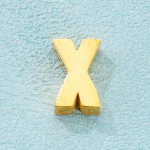 Vue macro d'un pendentif lettre X en métal doré 3D sur un fond bleu clair texturé