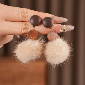Detail of vintage earrings with wood studs and beige faux fur pom-poms on golden links