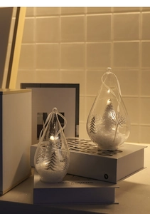 Macro detail of clear glass teardrop ornaments with snow cedar models and warm LED lighting