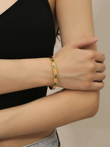 Detailed view of a gold-finish stainless steel cuff featuring green rhombus gemstones