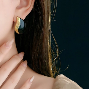Gros plan d'une boucle d'oreille huggie en or et émail vert foncé portée par un modèle