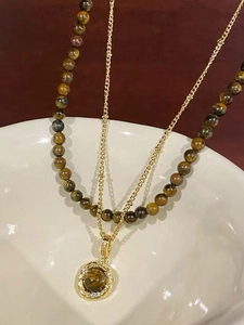 Detail of double-layer necklace with tiger eye beads and golden medallion pendant