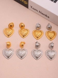 Detailed view of hammered heart earrings in gold and silver finishes on a pink surface