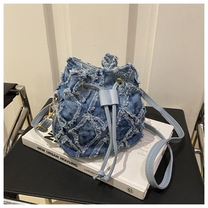 Close-up of light blue tie-dye denim bucket bag with metal hardware on a white book