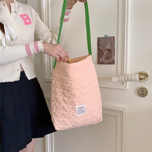 Pink quilted tote bag with green straps worn by model against a white door background