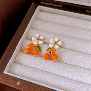 Macro view of gold-plated white flower earrings with orange fruit drops and green leaves