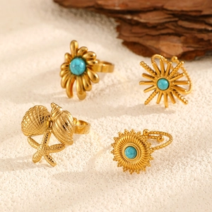 Detailed view of four golden bohemian rings with turquoise stones on sand and wood