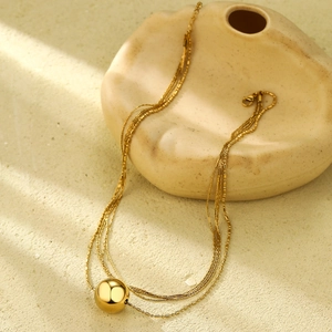 Detail of multilayered gold ball pendant necklace draped on minimalist ceramic art piece