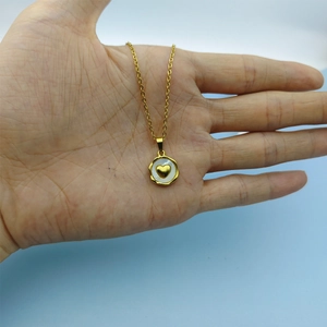 Detailed shot of a gold heart pendant with a white shell inlay held in hand