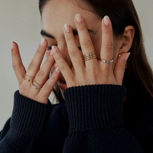 Close-up of minimalist gold and silver rings stacked on fingers with knitwear background