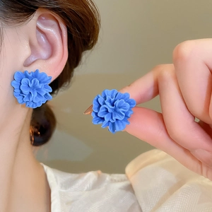 Detailed macro view of a blue resin flower stud earring worn on ear with soft lighting