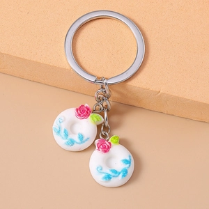 Detail of metal keychain with white round charms featuring pink roses and blue vine patterns