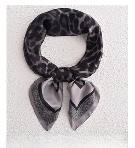 Detail of square satin scarf with leopard print and geometric patterns tied in a neat knot