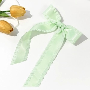 Detail of mint green satin bow hair clip with ruffled edges and long flowing ribbons