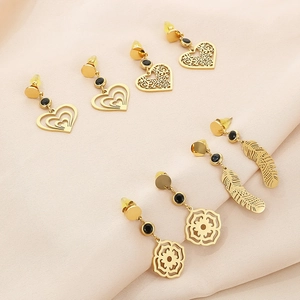 Détail de boucles d'oreilles plume et cœur en or avec gemmes noires sur tissu rose