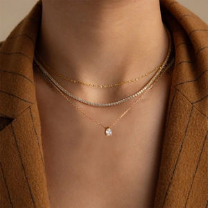 Detailed view of layered gold necklaces with pear-cut crystal and tennis chain on model