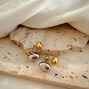 Detail of bicolor gold and silver bean-shaped earrings on stone background with silk
