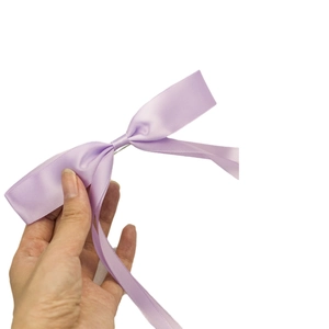 Elegant purple satin ribbon bow hair clip with long streamers held by a hand