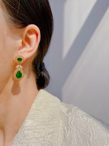 Detail view of emerald green teardrop earrings with gold textured edges on a model