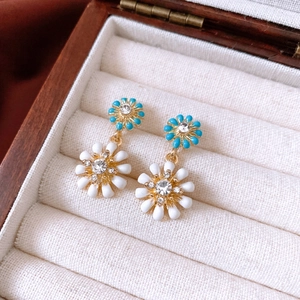 Gros plan de boucles d'oreilles fleurs bleu et blanc avec cristaux dans un écrin