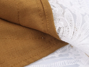 Detailed close-up of brown textured fabric stitched with delicate white lace trim