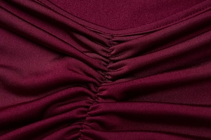Macro detail of wine red backless dress showing pleated fabric texture and stitching
