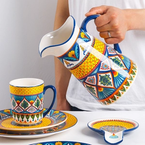 Hand-painted ceramic pitcher pouring water into a mug with matching plates and spoon rest