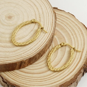 Close-up of golden oval earrings with honeycomb texture on a wooden background
