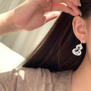 Detail of silver heart earring with turquoise gemstone worn on ear with natural lighting